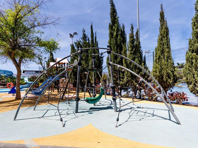 Modern speelterrein met glijbaan, schommels en klimrek onder een heldere hemel.
