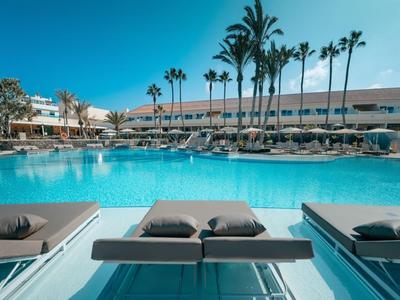 Hotelpool mit bequemen Liegen und hohen Palmen bei klarem Himmel.
