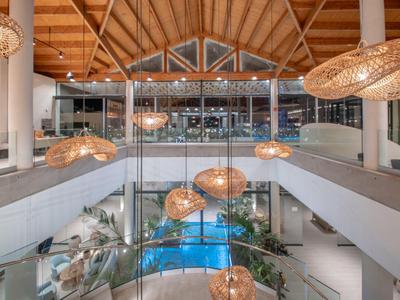 Moderner Hotelinnenbereich mit Pool und hängenden Lampen unter Holzdachstruktur.