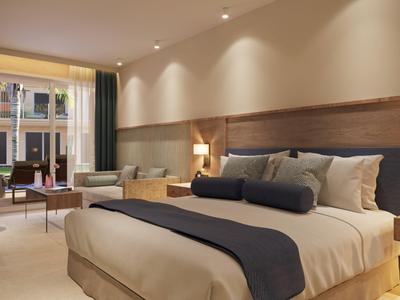Modern eingerichtetes Hotelzimmer mit großem Bett, Sofa und Fenstern mit Blick auf Innenhof.