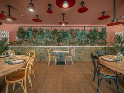 Modernes Restaurant mit Holzstühlen, Tischen und grüner Wanddekoration in warmem Ambiente.
