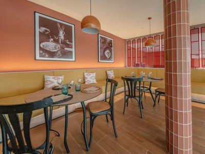Modern eingerichteter Hotel-Loungebereich mit orangenen Wänden, Holztischen und Sitzbänken.