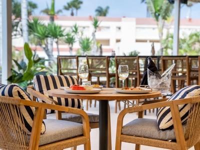 Gemütliche Sitzgruppe mit Korbstühlen und gestreiften Kissen auf Hotelterrasse mit Blick auf Palmen.