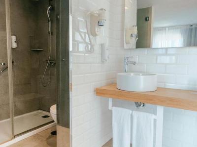 Baño moderno con ducha de vidrio, lavabo blanco y estante de madera clara.
