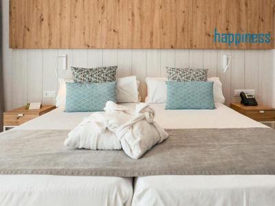 Habitación de hotel moderna con cama grande, manta gris, almohadas azules y dos albornoces blancos.