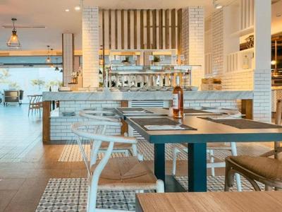 Restaurante moderno y luminoso con mesas de madera y vista al mostrador de cocina.