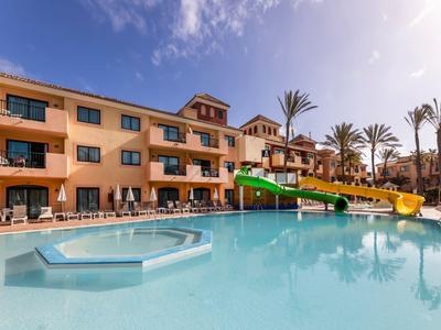 Gran piscina de hotel con tobogán, sombrillas y palmeras bajo cielo despejado.