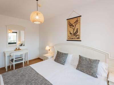 Dormitorio con cama doble, cojines grises, escritorio blanco y decoración minimalista en la pared.