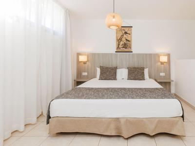 Habitación de hotel moderna con cama grande, cortinas blancas y iluminación sutil.