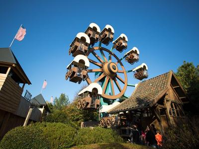 Freizeitpark mit kleinem Riesenrad und Holzgebäuden unter klarem blauem Himmel