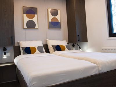 Modernes Schlafzimmer mit zwei Einzelbetten, weißen Bettlaken, dunkelbraunen Möbeln und abstrakter Wandkunst.