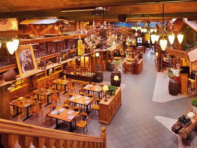 Großes rustikales Restaurant mit Holzmöbeln, warmem Licht und dekorativem Landhausstil.