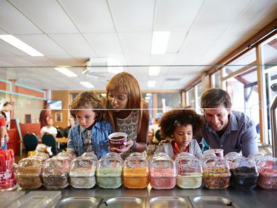 Kinder und Erwachsener wählen Süßigkeiten aus vielen bunten Glasbehältern in einem Laden.