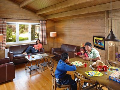 Inneneinrichtung eines Holzhauses mit zwei Erwachsenen und zwei Kindern beim Spielen und Entspannen.