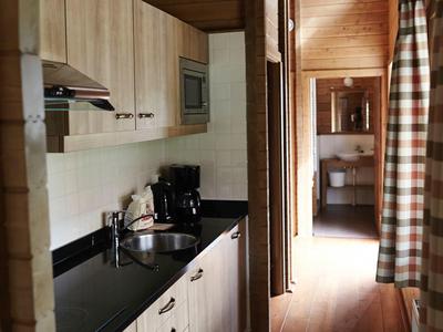 Schmale Küche mit Holzvertäfelung, schwarzen Arbeitsflächen und Geräten, helles Holz am Boden.