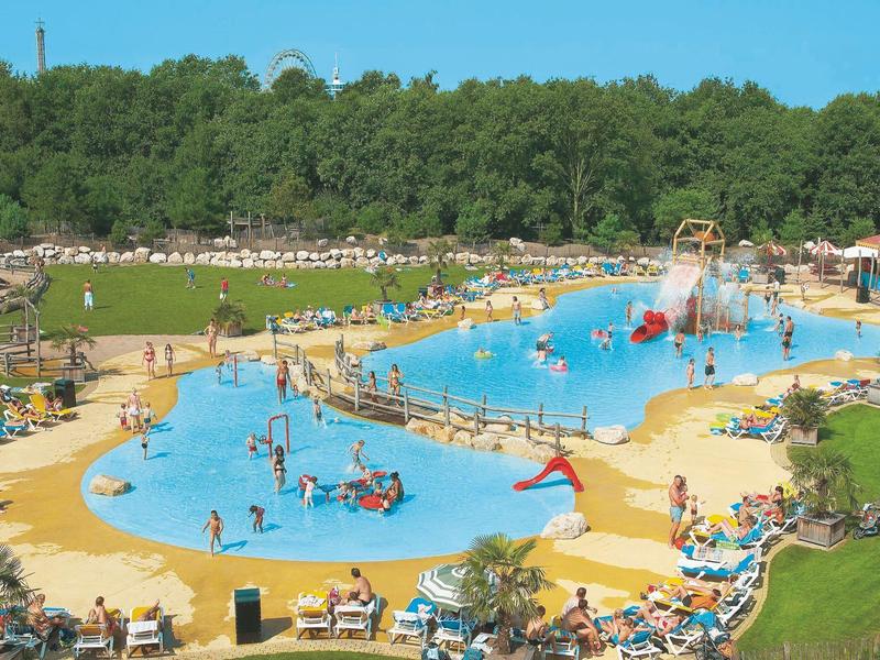 Großer Außenpool mit vielen Menschen, Liegestühlen und grasbewachsenem Hügel im Hintergrund.