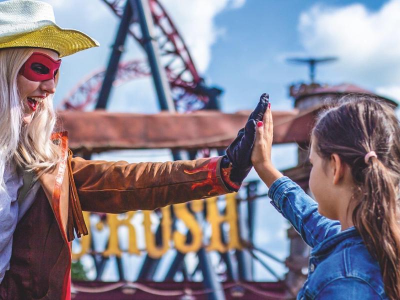 Zwei Menschen, einer als Cowboy verkleidet, klatschen sich vor einem Freizeitpark ab.
