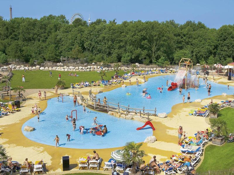 Freizeitpark mit großen blauen Wasserbereichen, Rutschen, Spielgeräten und vielen Besuchern im Grünen.