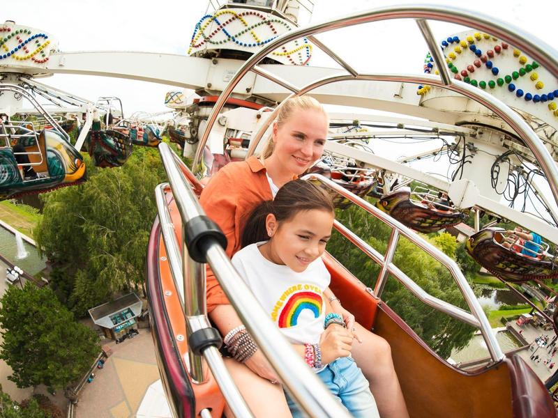 Zwei Mädchen sitzen lachend in einer bunten Freizeitpark-Fahrt mit Metallstreben und Mustern.
