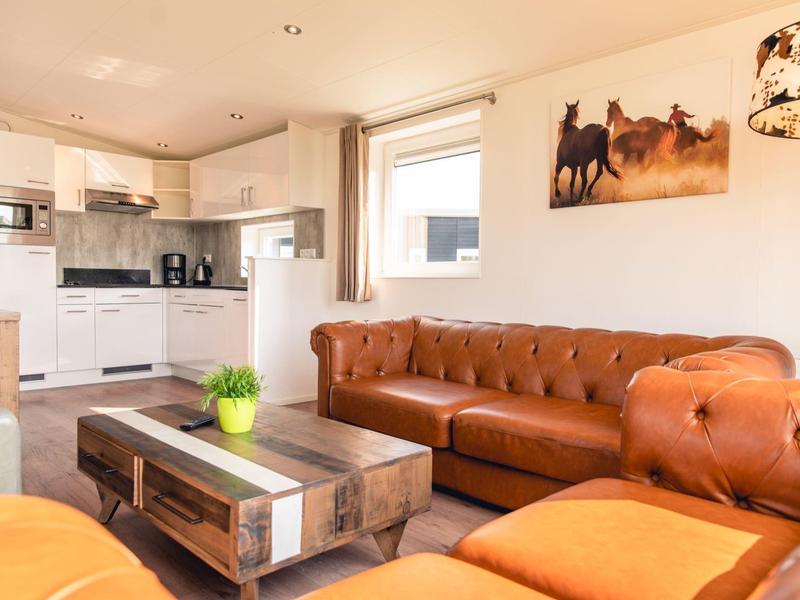 Helles Wohnzimmer mit braunen Ledersofas, rustikalem Holztisch und moderner weißer Küchenzeile.