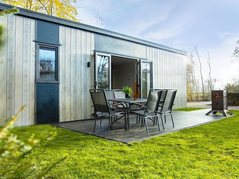 Modernes Holzhaus mit großer Glasschiebetür, Terrasse mit Tisch und Stühlen, umgeben von grünem Rasen.