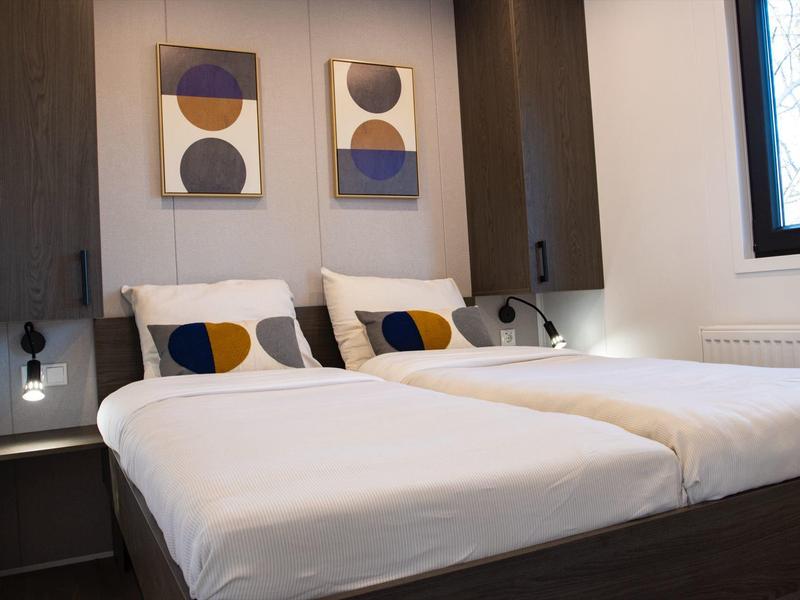 Modernes Schlafzimmer mit zwei Einzelbetten, weißen Bettlaken, dunkelbraunen Möbeln und abstrakter Wandkunst.