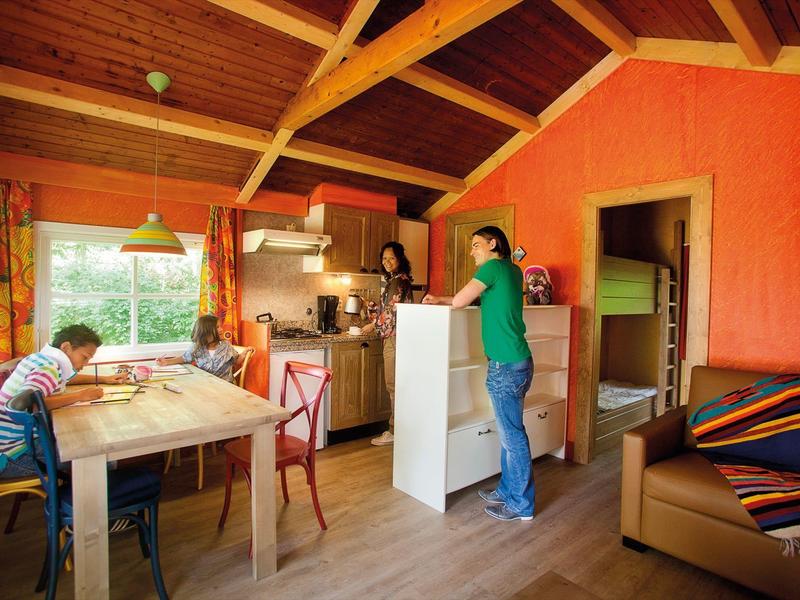 Gemütliche Küche mit Holzbalkendecke, orangenen Wänden und zwei Personen beim Essen und Kochen.