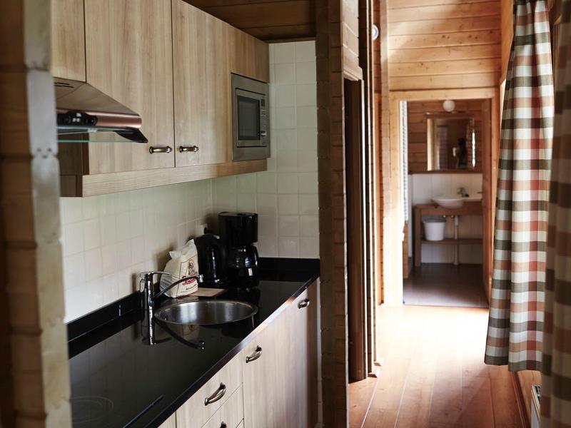 Schmale Küche mit Holzvertäfelung, schwarzen Arbeitsflächen und Geräten, helles Holz am Boden.