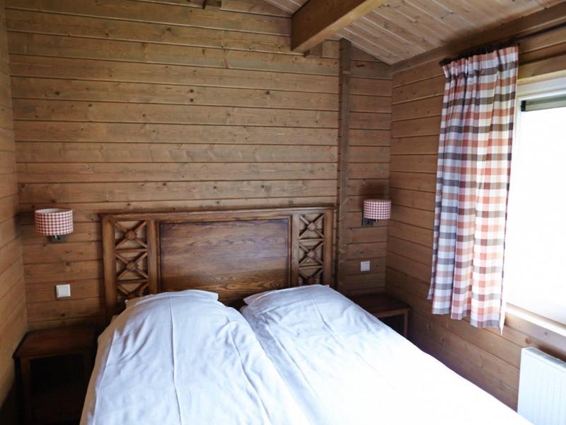 Kleines Schlafzimmer mit Holzverkleidung, Doppelbett, zwei Nachttischen und karierten Gardinen am Fenster.