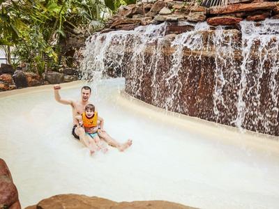 Zwei Personen entspannen im Pool mit Wasserfall und Felsen im Hintergrund.