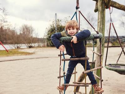 Ein Kind klettert auf einem Klettergerüst auf einem Spielplatz mit Sandboden.