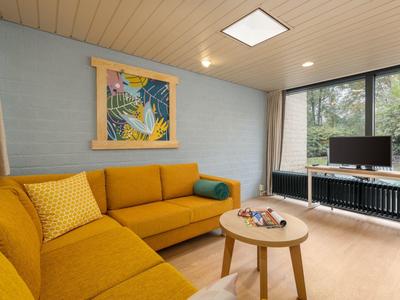 Cozy living room with yellow corner sofa, small wooden table, and large window with TV.