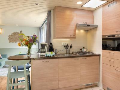 Compact modern kitchen with wooden cabinets in open living area with dining table and sofa zone.
