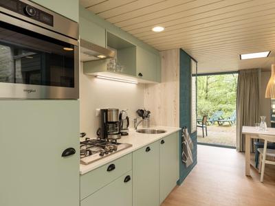 Modern pastel green kitchenette with coffee machine and view of terrace.