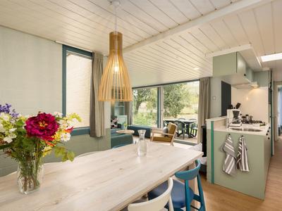 Bright dining area with wooden table, flowers, and modern kitchen with green cabinets in a vacation home.