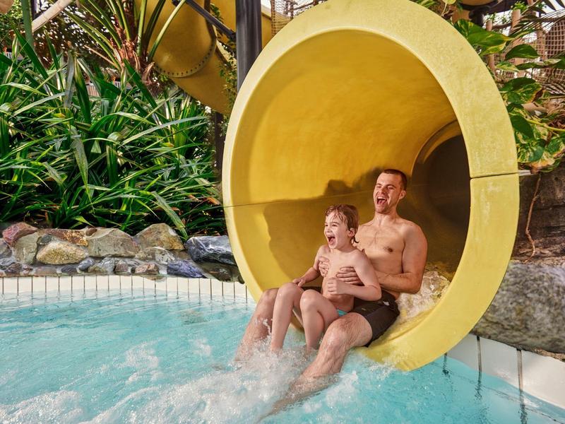 Father and son enjoying a water slide that ends in a pool.
