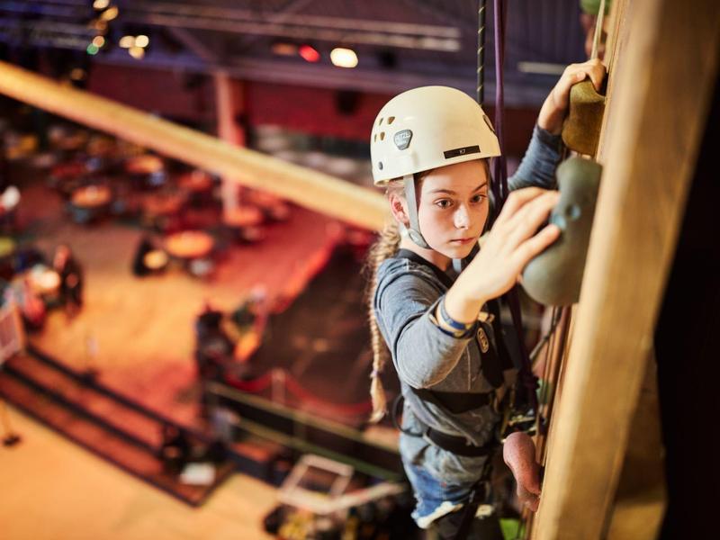 Young climber with helmet and safety harness on an indoor climbing wall