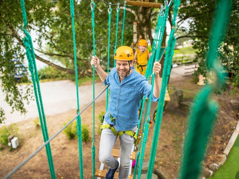 Two men wearing helmets climbing in a ropes course with ropes and platforms.