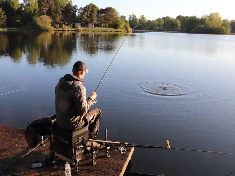 Person sitting on a pier fishing at a calm lake under sunny weather.