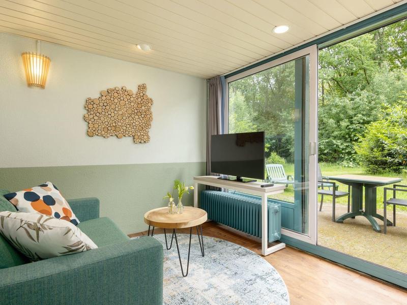 Cozy living room with green sofa, TV, and access to terrace with garden view.