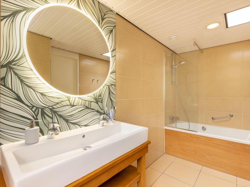 Modern bathroom with large mirror, double sink, and bathtub with glass partition.