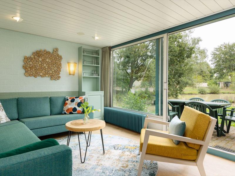 Living room with green sofa, wooden chair, and large windows overlooking garden.