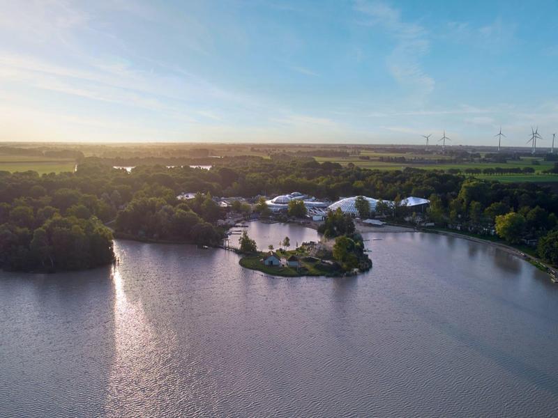 Aerial view of a calm lake with a small island and wind turbines on the horizon at sunset.