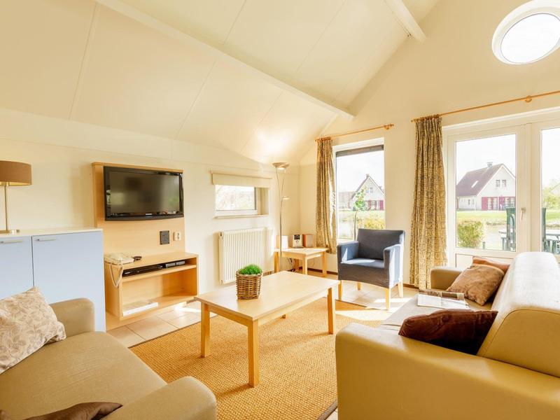 Lichte woonkamer met sofa's, tv, stoelen en grote ramen met uitzicht op de tuin.