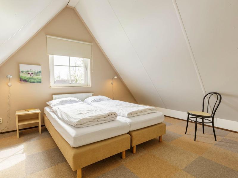 Lichte zolder slaapkamer met tweepersoonsbed, twee nachtkastjes en een stoel.