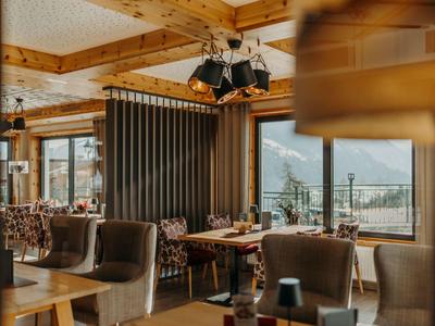 Gemütlicher Gastraum mit Holzbalken, Sesseln und großen Fenstern mit Bergblick.
