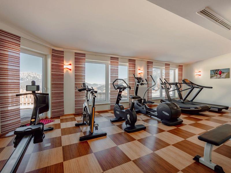 Nowoczesna siłownia z urządzeniami treningowymi i dużymi oknami z widokiem na miasto.