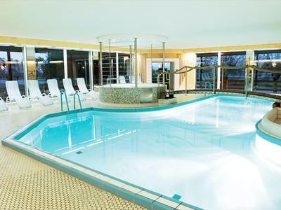 Hallenbad mit Liegestühlen und Whirlpool in einem hellen Raum mit großen Fenstern.