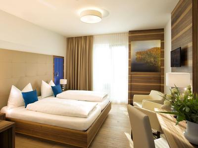 Jasny pokój hotelowy z dwoma łóżkami pojedynczymi, częścią wypoczynkową i dużym oknem z zasłonami.