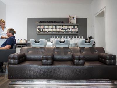 Nowoczesne wnętrze salonu fryzjerskiego z umywalkami i skórzaną sofą na pierwszym planie.